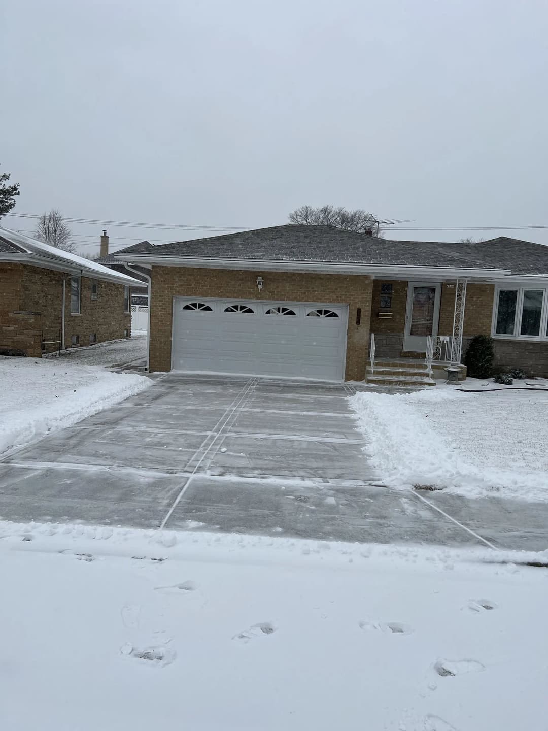 Snow-covered residential house with a clear driveway and garage in winter.