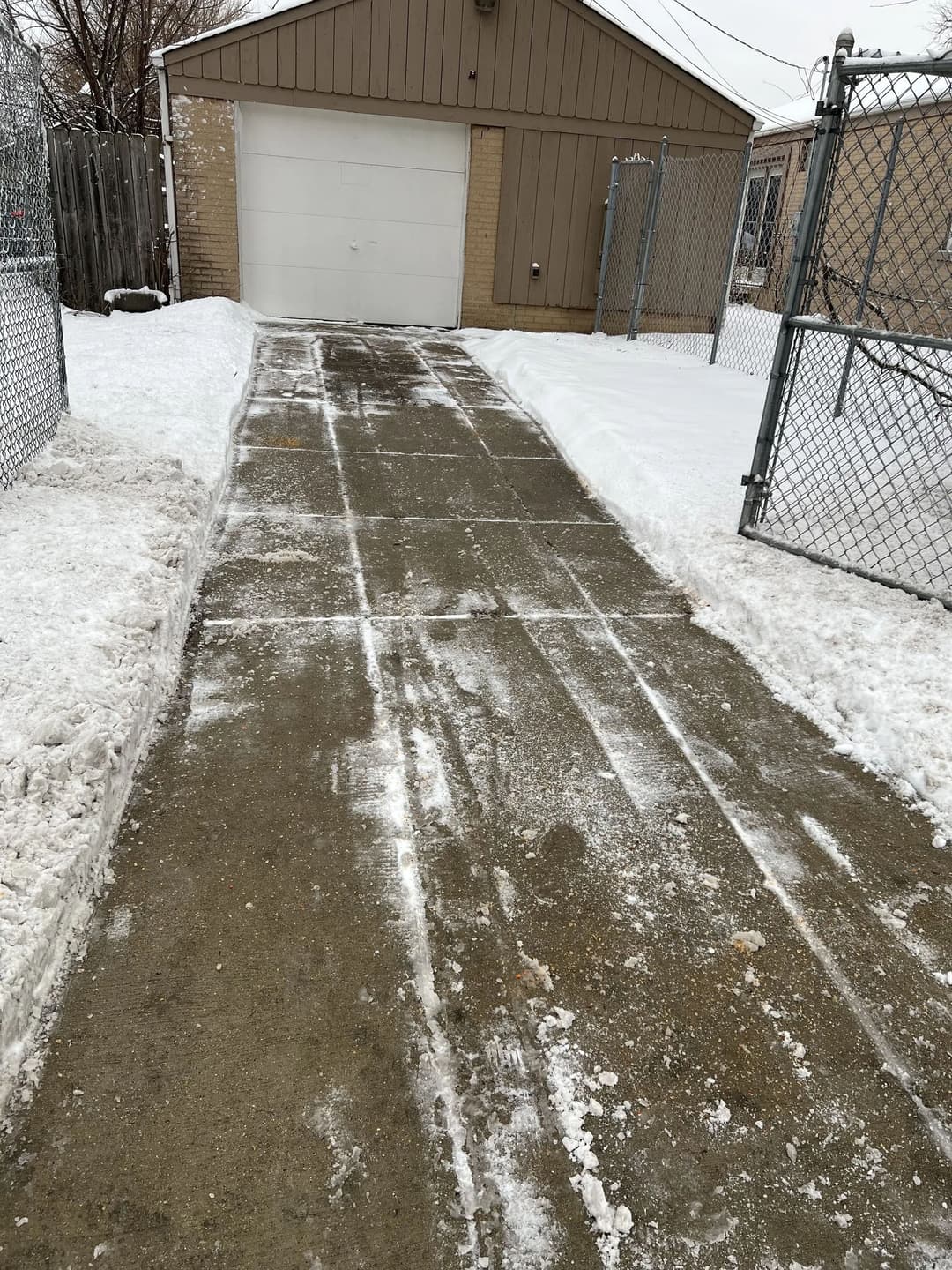 Clear driveway with snow on both sides leading to a garage in winter.