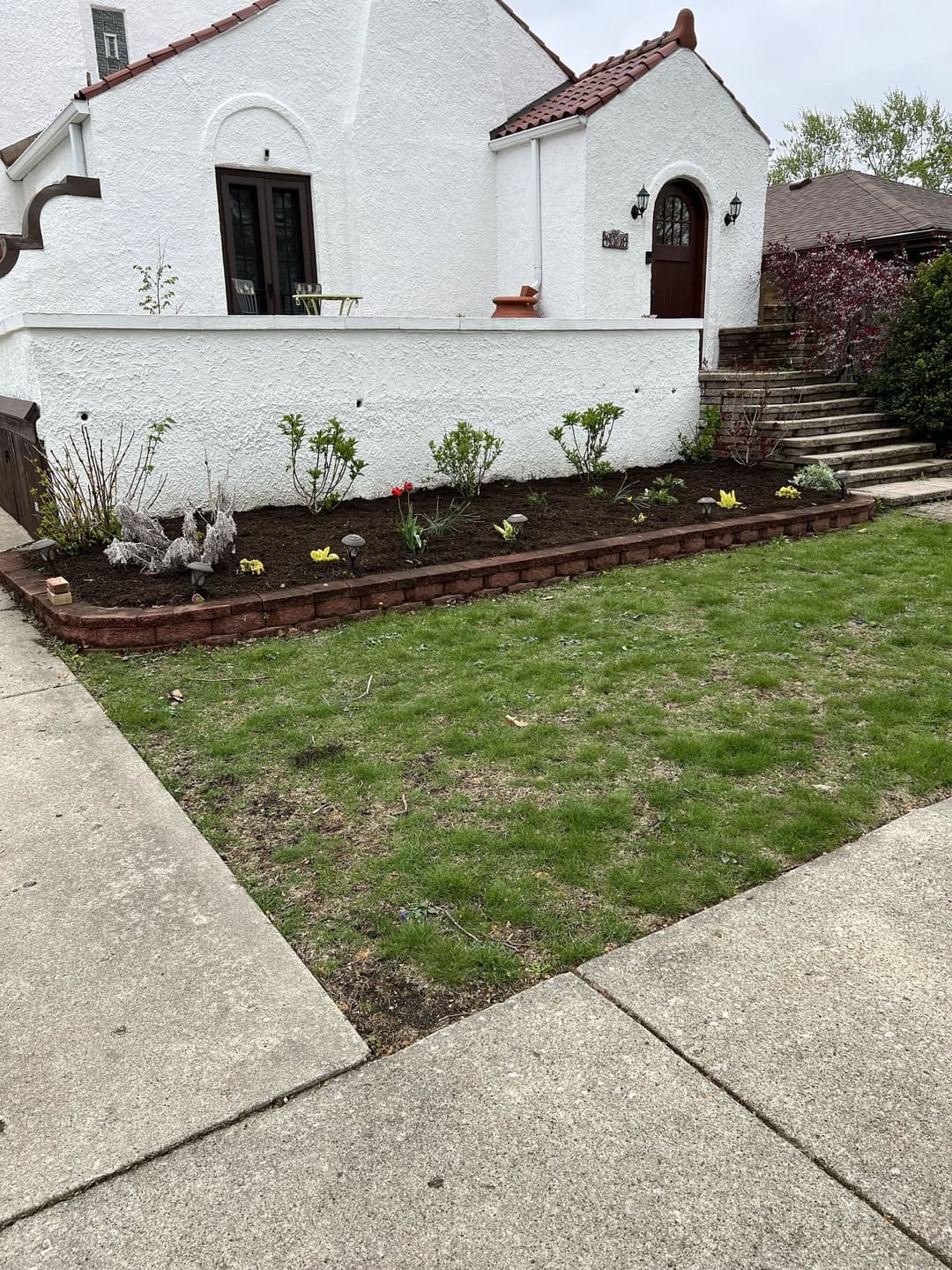 Well-maintained garden bed with flowers and shrubs next to a white house and pathway.