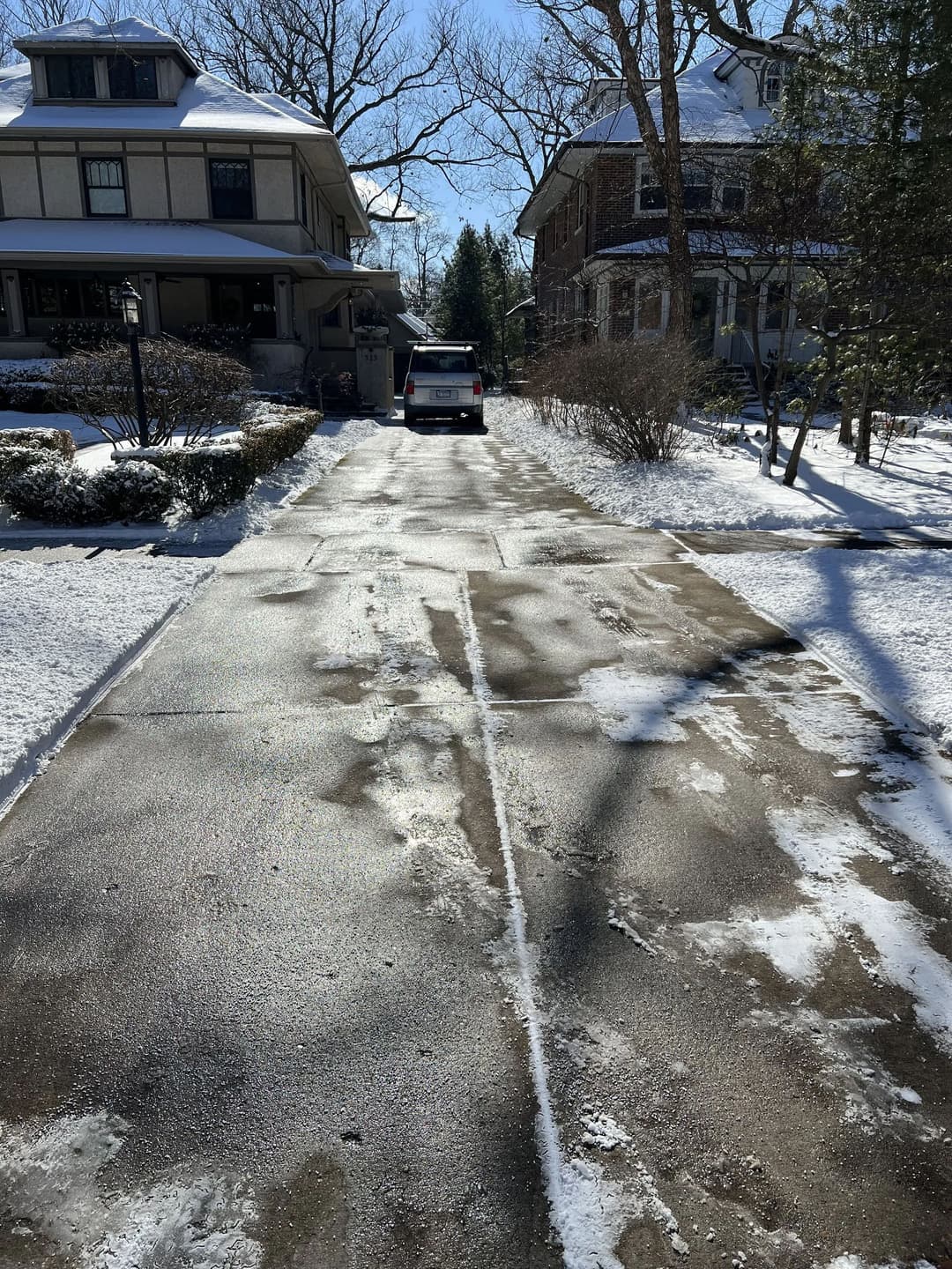 Snow-covered driveway with tire tracks and parked vehicle on a sunny winter day.