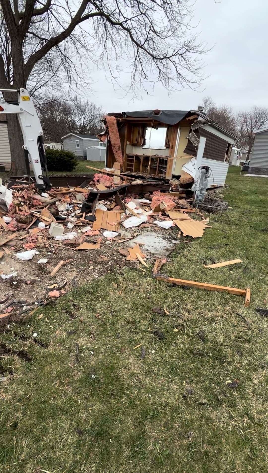 Damaged shed debris scattered on grass, with construction machinery nearby.