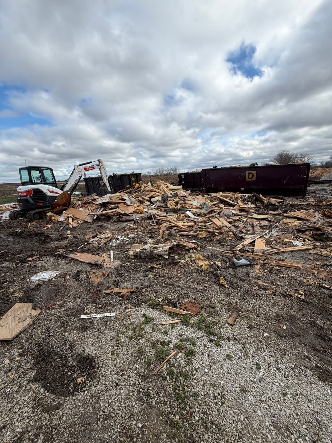 Debris field with construction waste and machinery in a cloudy outdoor setting.