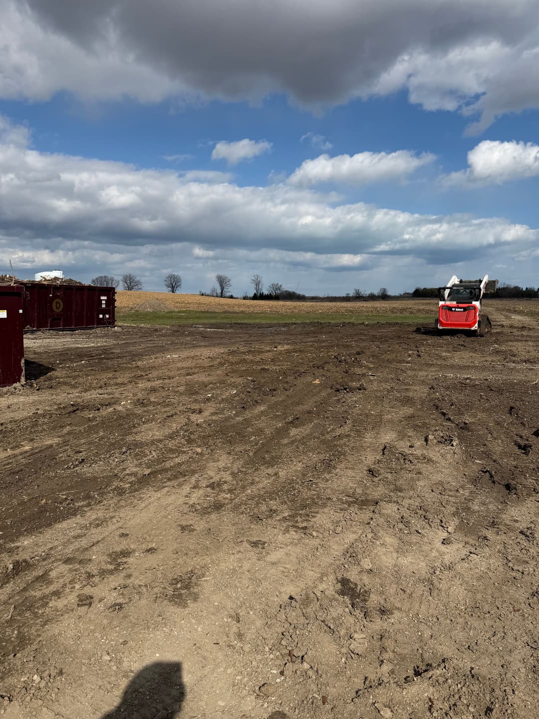 Red tractor working on a cleared field under a cloudy sky with scattered containers.
