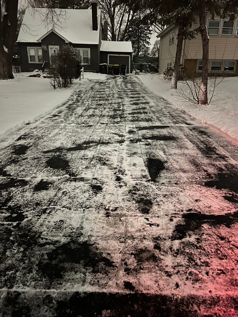 Cleared snow-covered driveway leading to a house in winter setting.